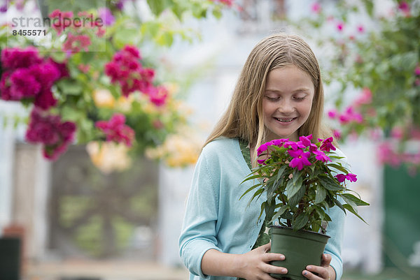 Eine Bio-Blumenpflanzengärtnerei. Ein junges Mädchen hält eine blühende Pflanze.