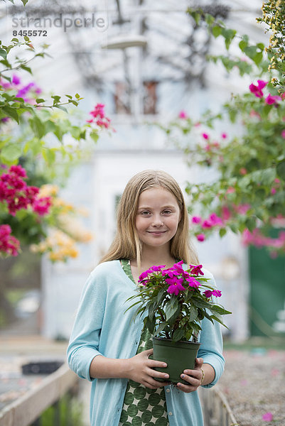 Eine Bio-Blumenpflanzengärtnerei. Ein junges Mädchen hält eine blühende Pflanze.