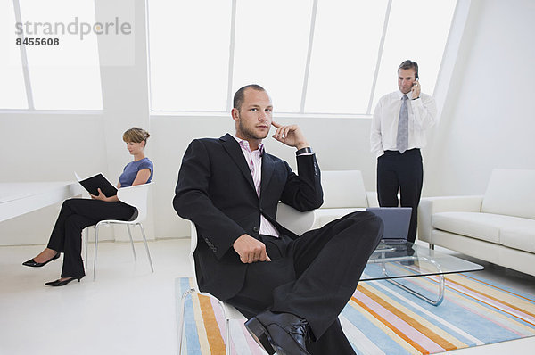 Drei Geschäftsleute in einem Büro  einer am Telefon  einer  der an einem digitalen Tisch arbeitet  und einer  der auf einem Stuhl sitzt.