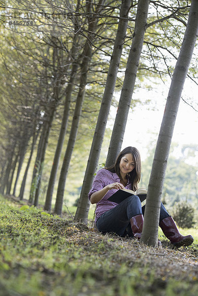 Eine Frau sitzt unter den Bäumen und liest ein Buch.