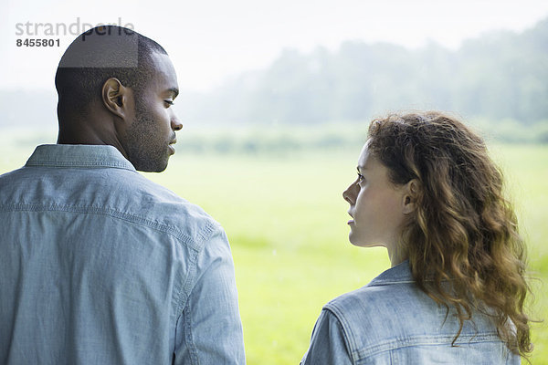 Ein junger Mann und eine junge Frau  ein Paar nebeneinander stehend. Sie sehen einander an.