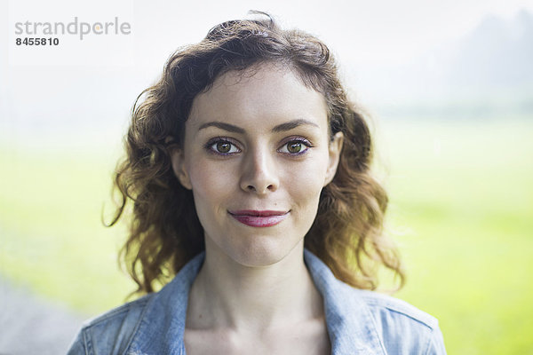Eine junge Frau in einer ländlichen Landschaft  mit vom Wind gelocktem Haar  lächelnd.