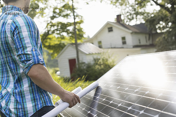 Ein Mann  der einen Plan zur Anbringung eines Solarpanels im Garten eines Bauernhauses verwendet.