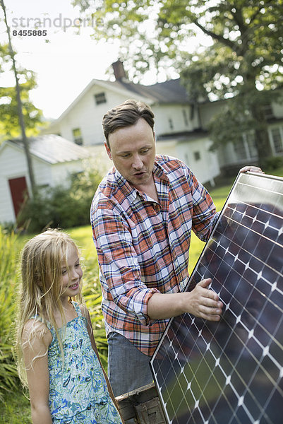 Ein Mann und ein junges Mädchen schauen auf eine Solaranlage in einem Garten.
