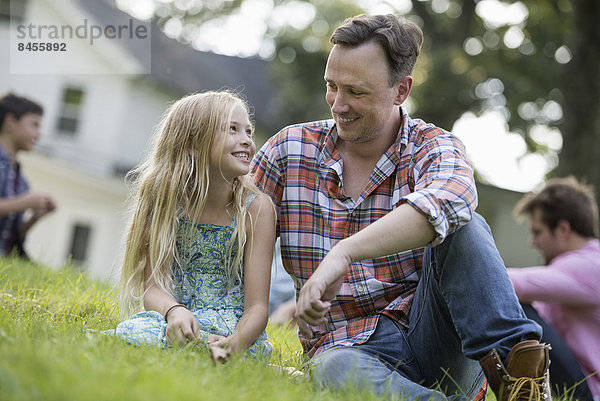 Ein Vater und eine Tochter auf einem Sommerfest  auf dem Rasen sitzend.