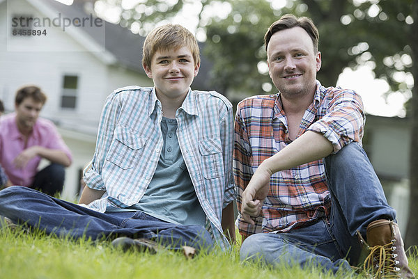 Ein Vater und sein Sohn bei einem Sommerfest  auf dem Rasen sitzend.