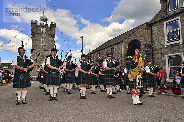 Eine Pipe Band  angeführt vom Pipe Major  vor dem Uhrturm im Zentrum  Dufftown  Moray  Highlands  Schottland  Großbritannien
