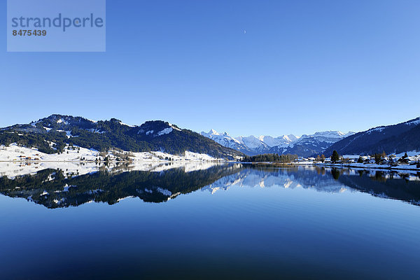 Schneebedeckte Berge spiegeln sich im Stausee Sihlsee im Hochtal von Einsiedeln  Schwyz  Schweiz