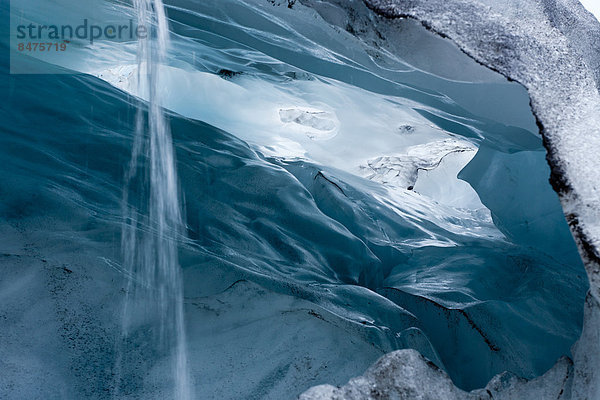 Einblick in eine blaugrüne Eishöhle mit ablaufendem Tauwasser auf dem Skaftafell Gletscher  Island
