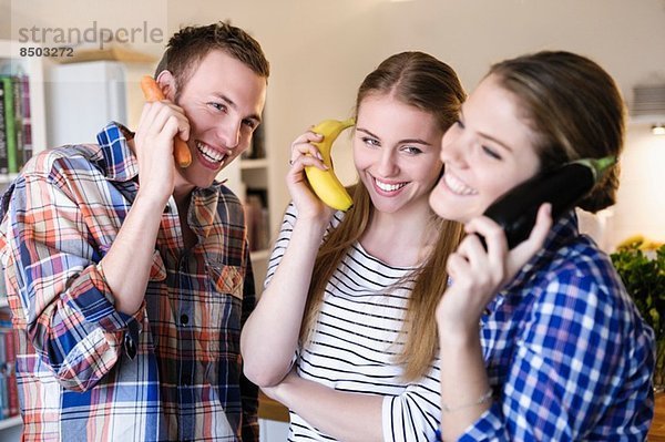 Drei junge Leute  die Spaß daran haben  Obst als Telefon zu benutzen.