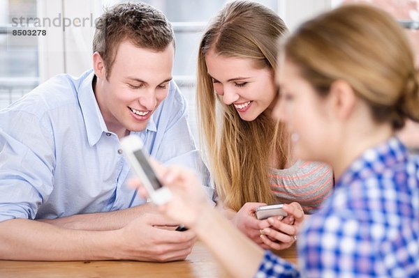 Drei junge Leute schauen auf Handys und lächeln