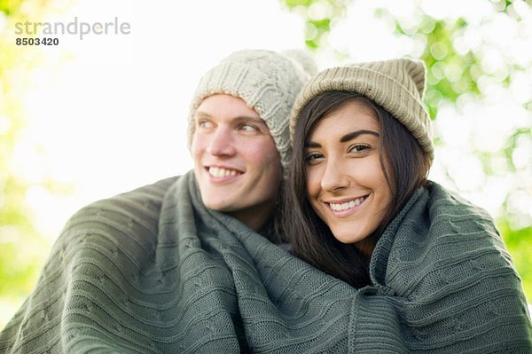 Junges Paar mit Strickmützen in Decke gehüllt