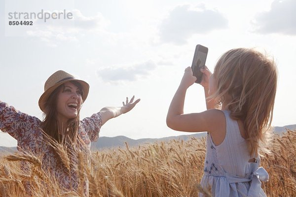 Mädchen fotografiert Mutter im Weizenfeld mit offenen Armen