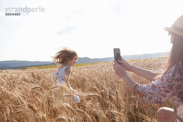 Mutter fotografiert Mädchen  die durchs Weizenfeld läuft
