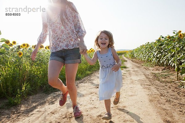 Mutter und Tochter laufen durch das Sonnenblumenfeld