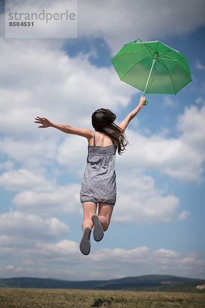 Mittlere erwachsene Frau mit grünem Regenschirm  springend