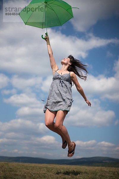 Mittlere erwachsene Frau mit grünem Regenschirm  springend