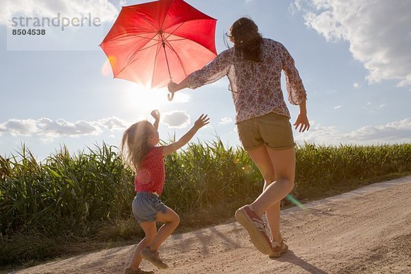 Mutter und Tochter gehen mit rotem Regenschirm durchs Feld.