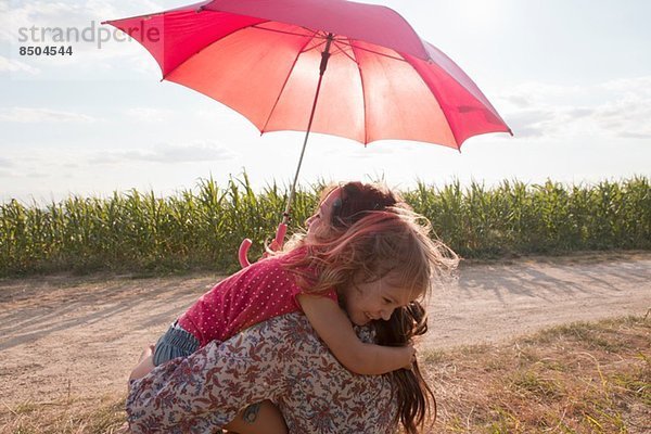 Mutter und Tochter umarmen sich unter rotem Regenschirm