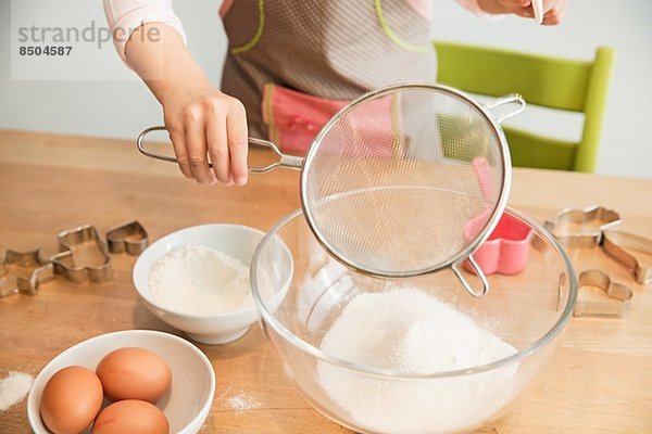 Mädchen siebt Mehl in die Rührschüssel