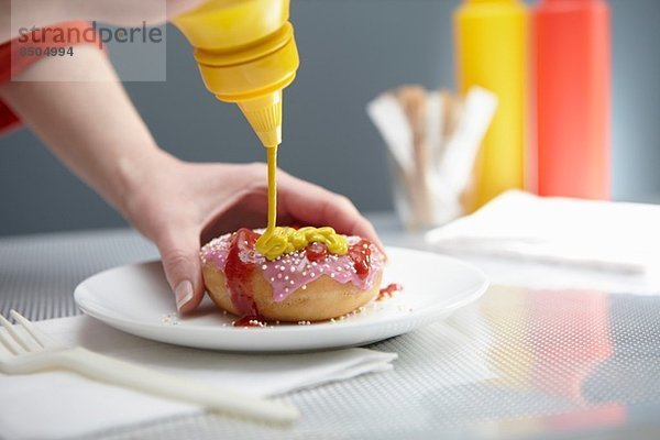 Frau spritzt Donut mit Ketchup und Senf