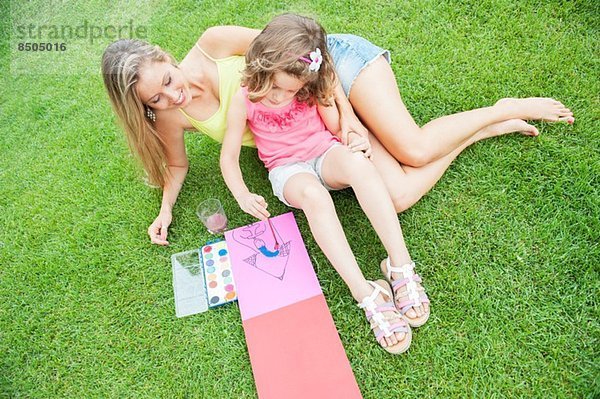 Mutter und Tochter malen  auf Gras sitzend