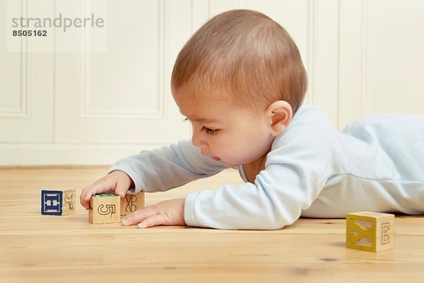 Baby liegt auf der Vorderseite und spielt mit Bausteinen