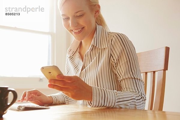 Junge Frau sitzt am Tisch und schaut auf das Smartphone.