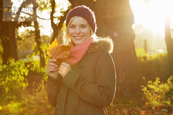 Porträt einer jungen Frau im Park mit Herbstblatt