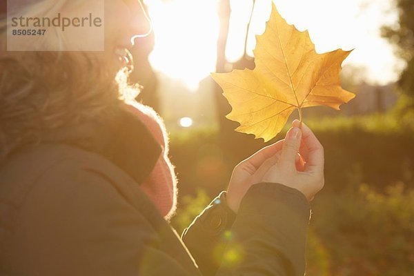 Porträt einer jungen Frau im Park mit Herbstblatt