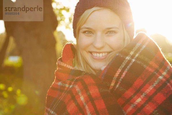 Porträt einer jungen Frau im Park  Tartan-Picknickdecke um die Schultern herum