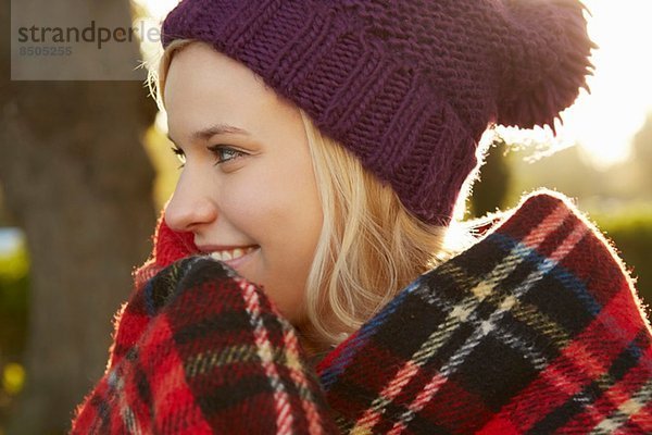 Porträt einer jungen Frau im Park  Tartan-Picknickdecke um die Schultern herum