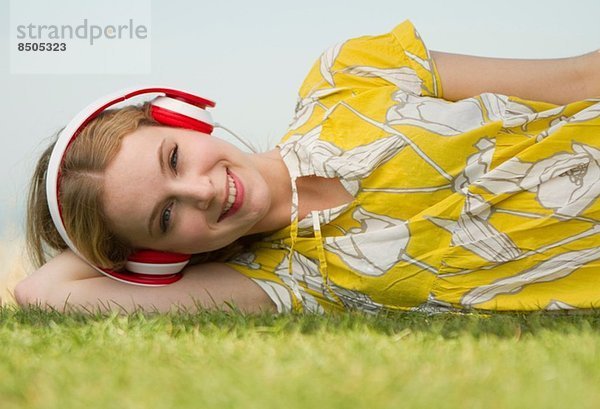 Porträt einer jungen Frau  die Kopfhörer auf Gras hört.