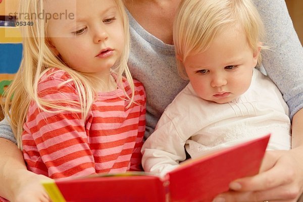 Mutter liest Bilderbuch mit zwei Töchtern