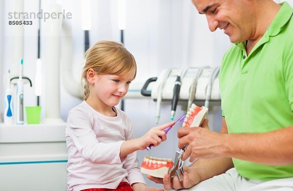 Zahnarzt lehrt Mädchen  wie man Zähne putzt