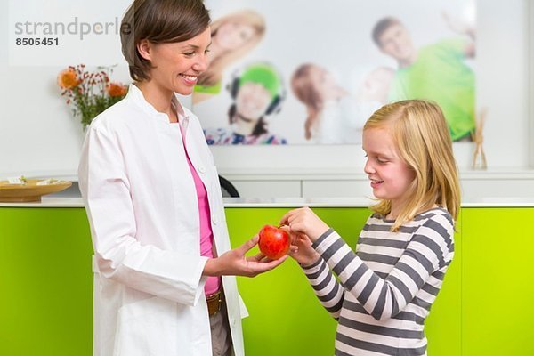 Zahnarzt gibt Mädchen Apfel in der Zahnarztpraxis