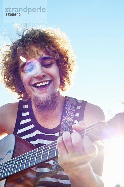 Junger Mann spielt Gitarre bei Sonnenschein