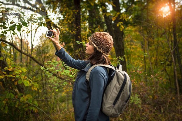 Reife Frau beim Fotografieren im Wald mit dem Smartphone