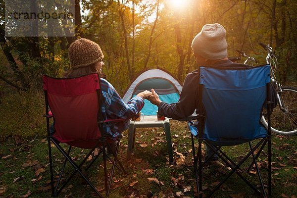 Erwachsenes Paar  das auf Campingstühlen vor dem Zelt sitzt und Händchen hält.