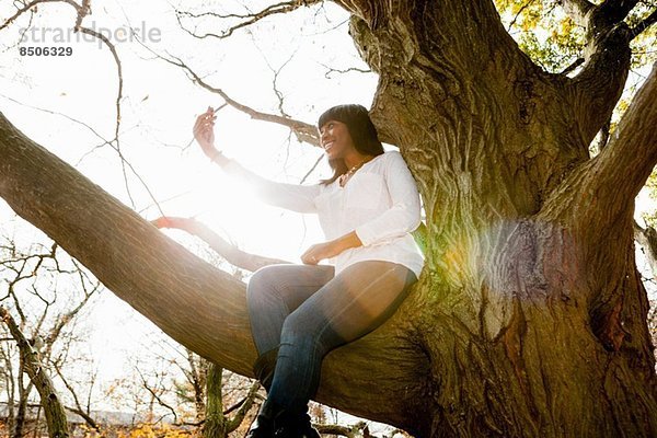 Junge Frau beim Selbstporträt im Parkbaum sitzend