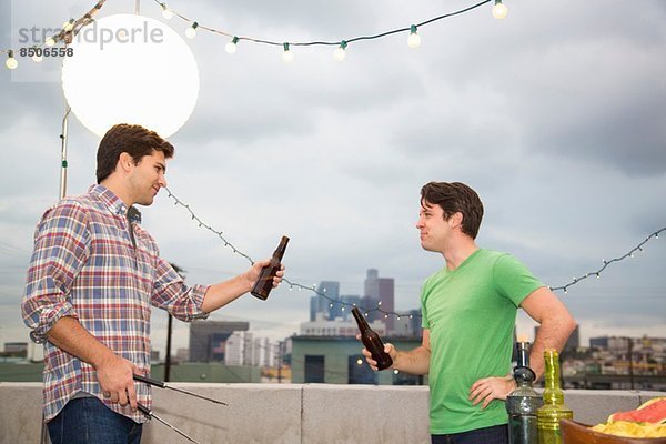 Zwei männliche erwachsene Freunde beim Grillen auf dem Dach