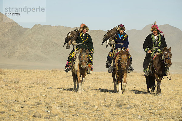 Drei kasachische Adlerjäger auf ihren Pferden auf dem Weg zum Adlerfest in Sagsai  Bayan-Ölgii Aimag  Mongolei