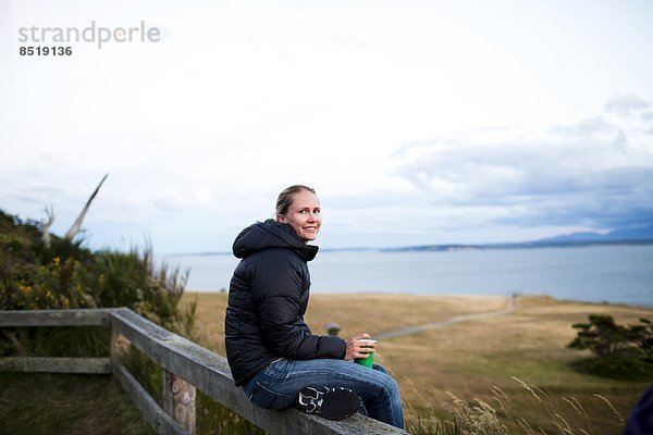 junge Frau junge Frauen Fröhlichkeit sitzend lächeln Küste Insel Blick in die Kamera Ansicht Geländer