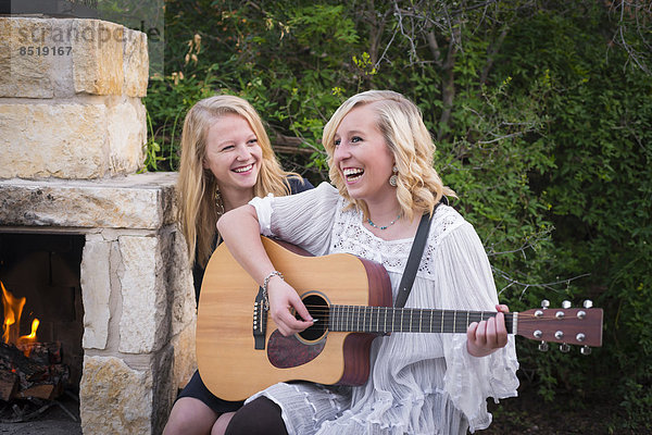 USA  Texas  Two happy teenage girls with guitar by the fireside