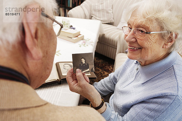 Seniorin zeigt ihrem Mann ein altes Foto von sich selbst