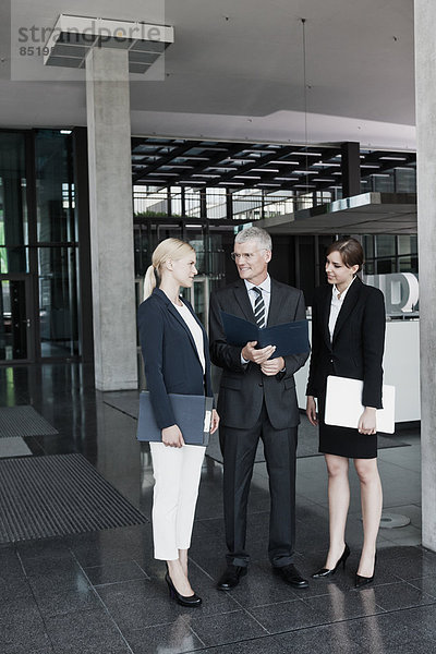 Three businesspeople with documents talking in office