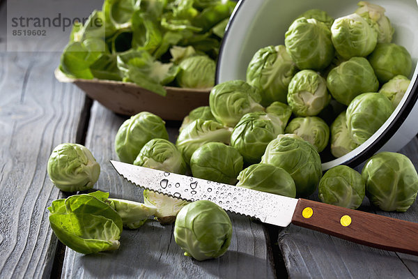Bowl of Brussels sprouts  plate with peels and kitchen knife on grey wooden table