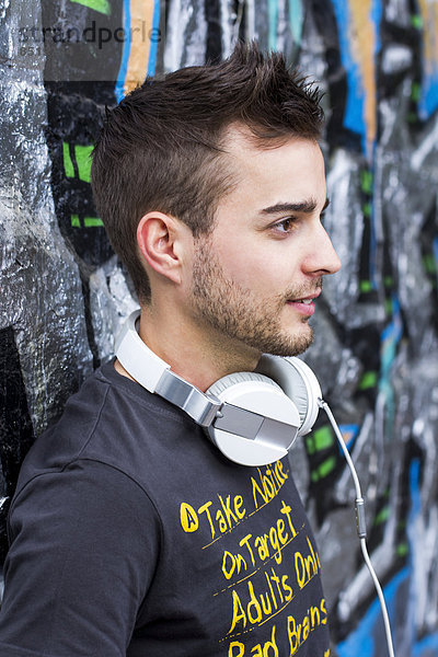Austria  Klagenfurt  Mid adult man with head phones in front of graffiti wall