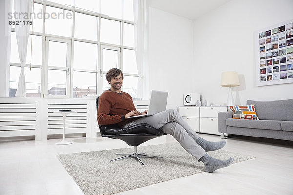 Mann zu Hause sitzend im Stuhl  mit Laptop