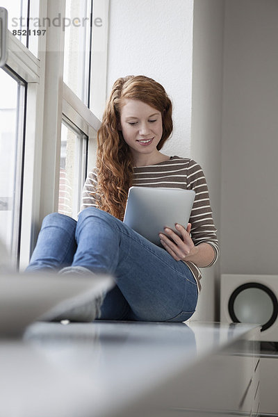 Frau auf Fensterbank sitzend  mit digitalem Tablett